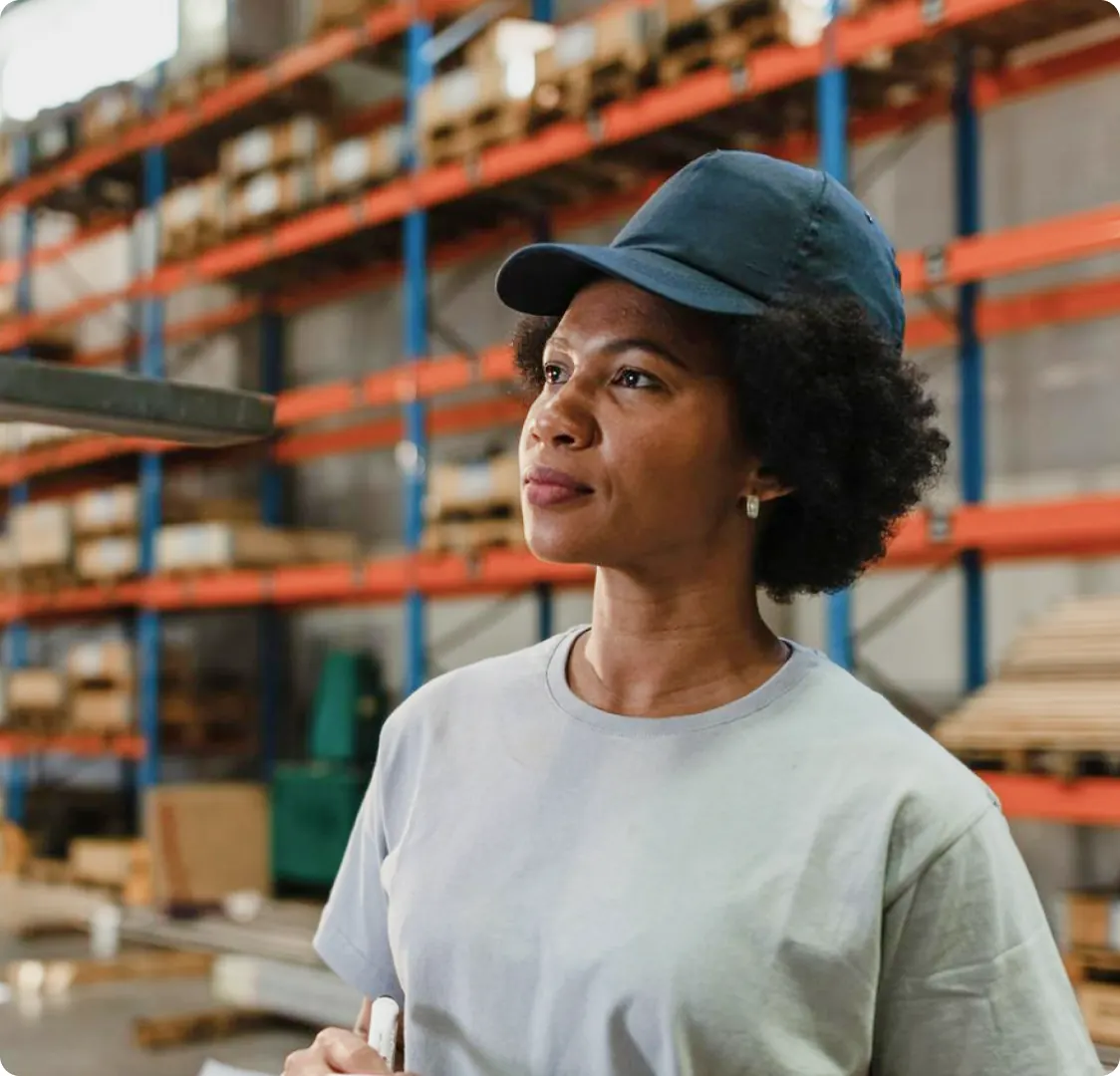 A photograph of a worker in a cap standing in a warehouse aisle in front of racked pallets.