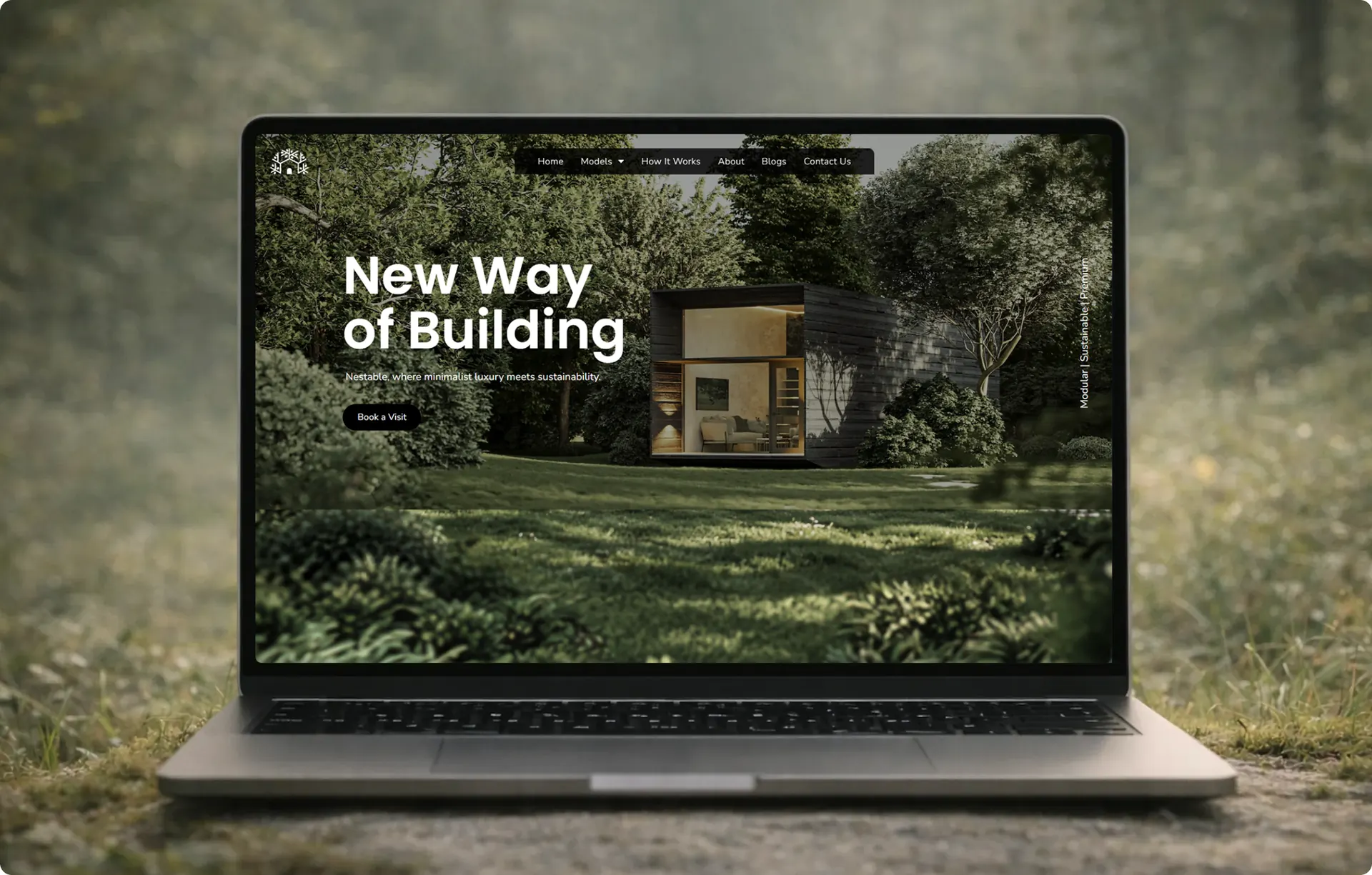 A laptop on grass in a forest clearing, showing the Nestable homepage with the headline New Way of Building over a photo of a dark timber cabin.