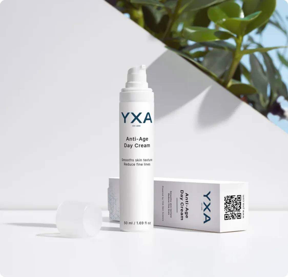 A YXA Anti-Age Day Cream bottle standing beside its box on a white surface, with a plant overhead and its lid lying to one side.