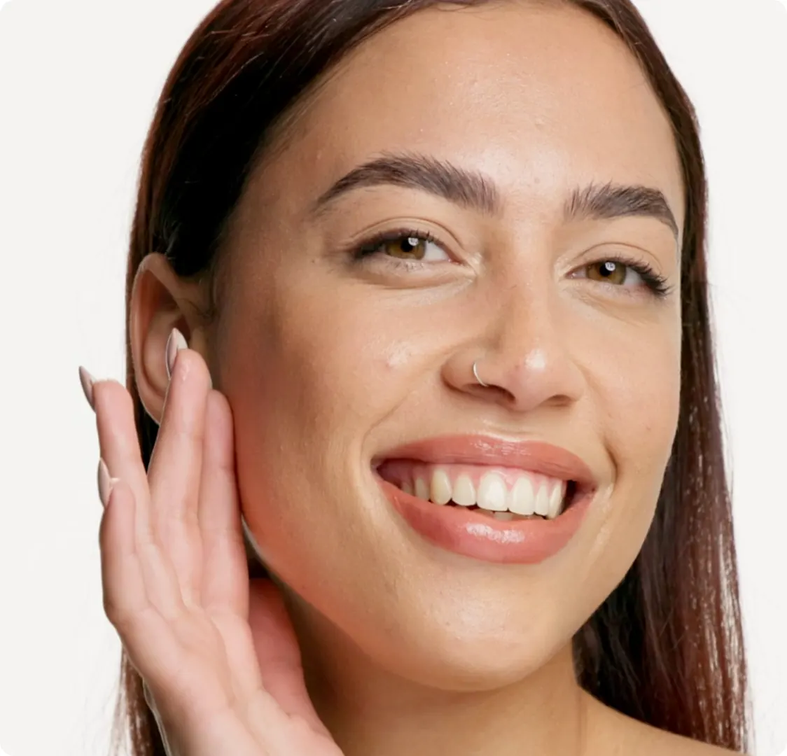 A woman smiling with her hand raised to her face, on a plain background.